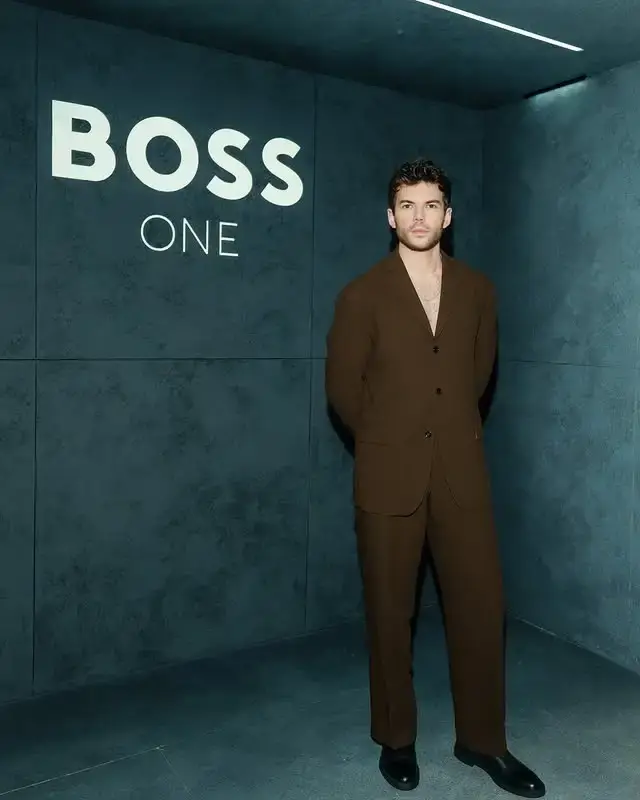 Luke Newton poses at the 2025 BOSS One: David Beckham party wearing a single-breasted brown blazer without a shirt underneath and matching brown trousers.