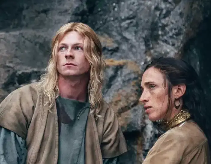 Stuart Campbell as Derfel and Ellie James as Nimue face each other in period costumes while standing in a rugged, grassy landscape in The Winter King.