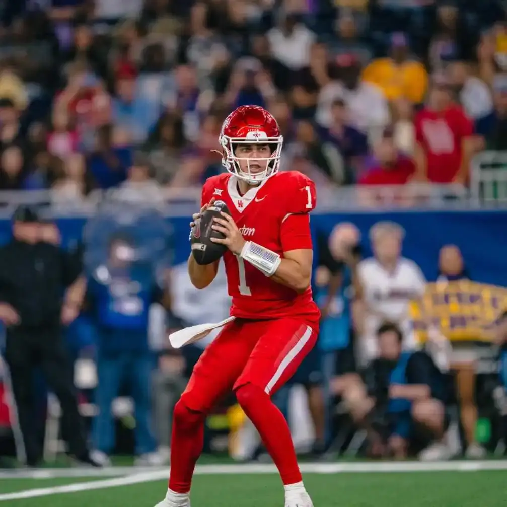 Conner Weigman wears a red University of Houston jersey and helmet while looking downfield to pass a football.
