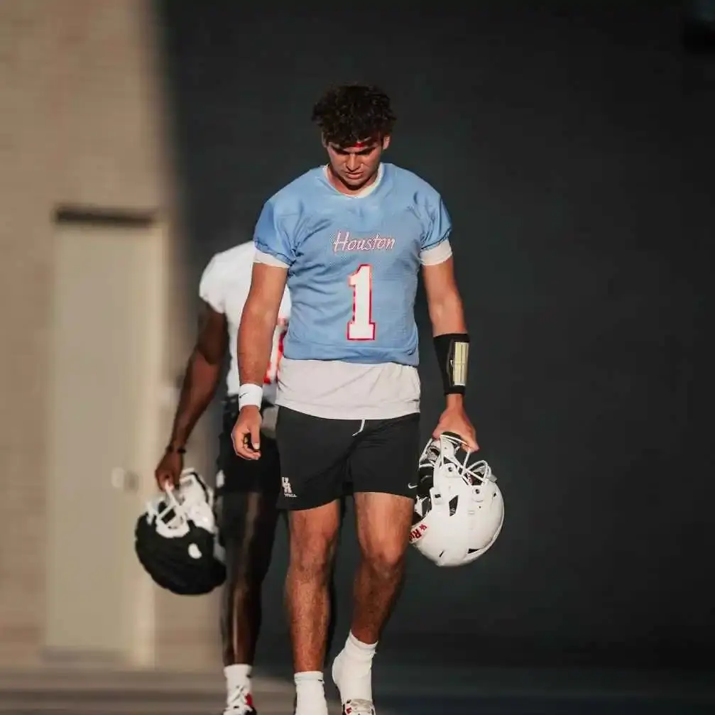 Conner Weigman, wearing a #1 jersey, holds a helmet in one hand while scanning the field during a game.