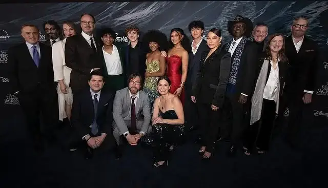 Actor Walker Scobell stands in the center of a large group of cast and crew members on a red carpet for a Disney+ production.