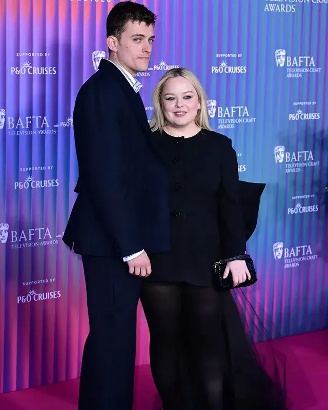 Jake Dunn and Nicola Coughlan pose together on a pink red carpet in front of a blue BAFTA backdrop wearing coordinated black formal attire.
