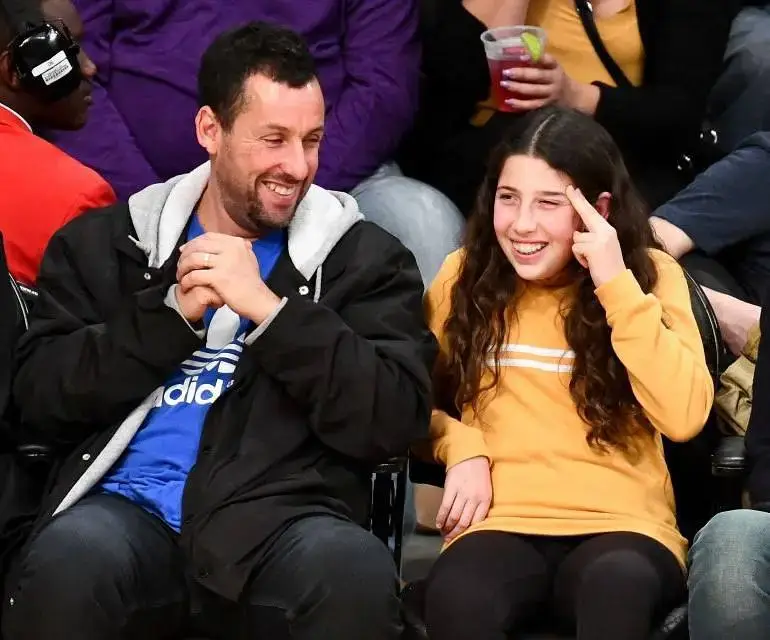 Adam Sandler and her daughter Sadie Sandler sat at a basketball game in courtside, smiling and laughing together in casual attire.