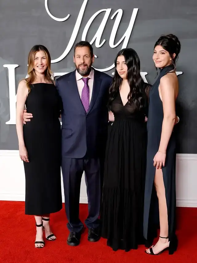 Sadie Sandler poses on a red carpet with her family wearing a floor-length black gown with sheer long sleeves.
