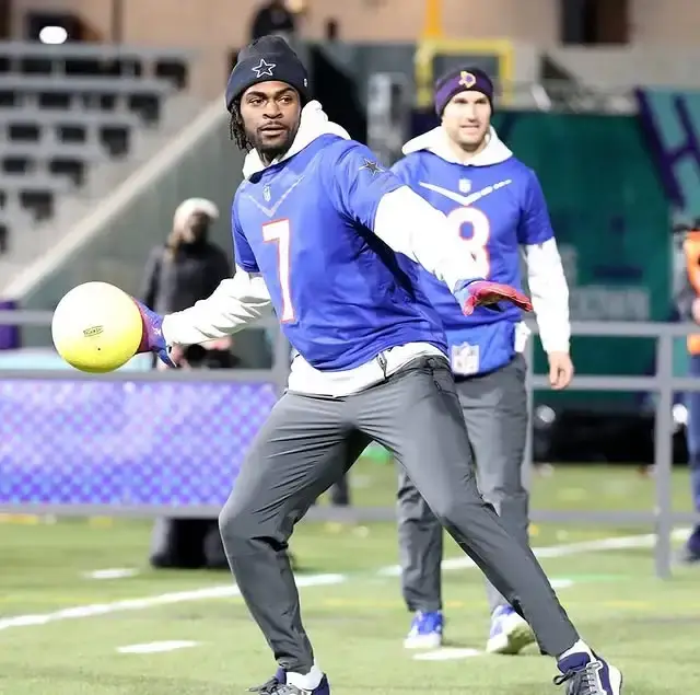 Trevon Diggs prepares to throw a yellow ball during a practice session while wearing a blue Dallas Cowboys jersey and a black beanie.