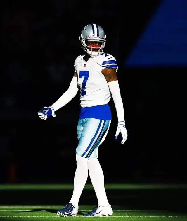 Trevon Diggs standing on a football field in a white and blue Dallas Cowboys uniform with his helmet on.