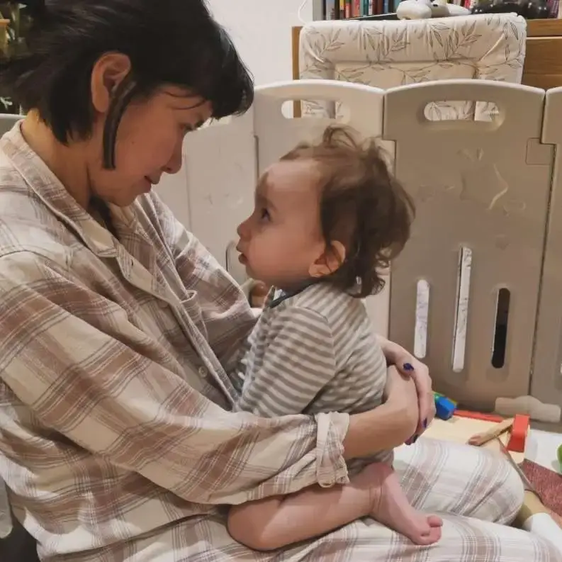 Actress Katie Leung sits on the floor and shares a tender moment while holding her young son in her lap.