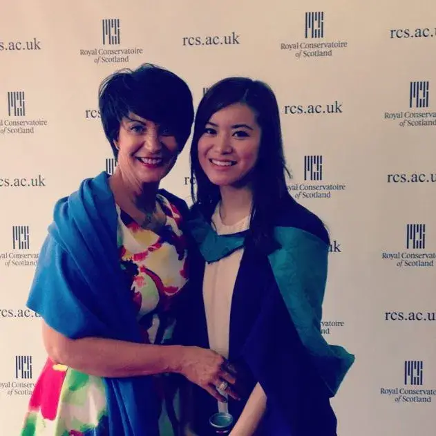 Actress Katie Leung smiles alongside her mother, Kar Wai Li Leung, while wearing graduation robes in front of a Royal Conservatoire of Scotland backdrop.