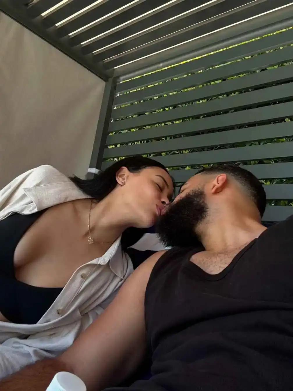 Desmond Scott and his ex-wife  Kristy Scott share a kiss while relaxing outdoors under a slatted pergola.