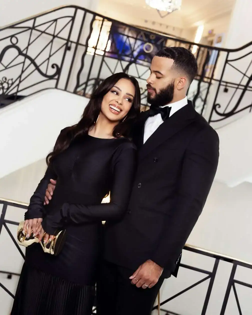 Desmond Scott and Kristy Scott pose elegantly on a grand staircase while wearing matching formal black attire.