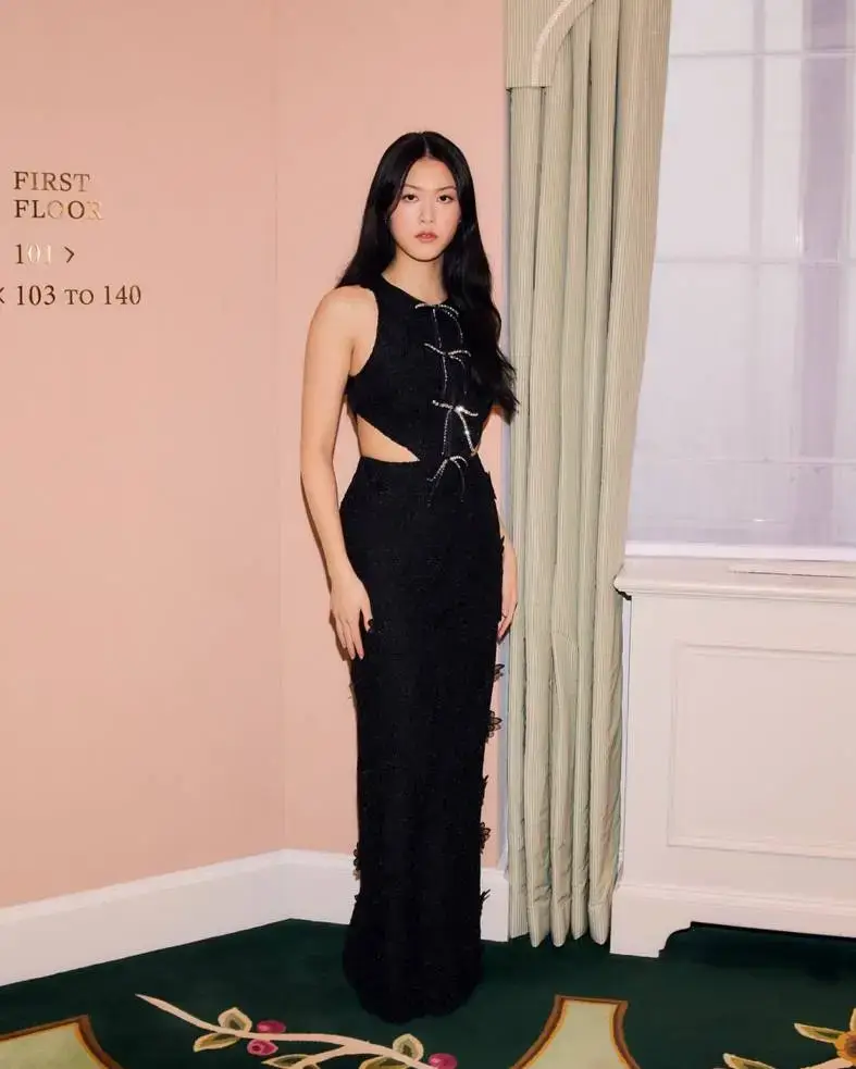 Isabella Wei stands elegantly in a hallway wearing a sleeveless black lace gown with side cutouts and bow details.