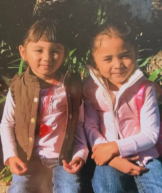 A childhood photograph shows Alyssa Thompson and Gisele Thompson sitting together outdoors while wearing matching pink shirts and layered vests.