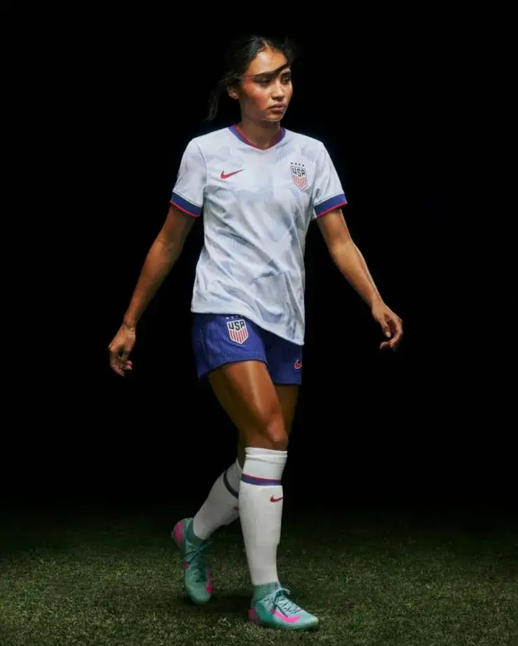 Alyssa Thompson stands confidently on a soccer pitch wearing a white United States national team jersey and blue shorts while looking off to the side.