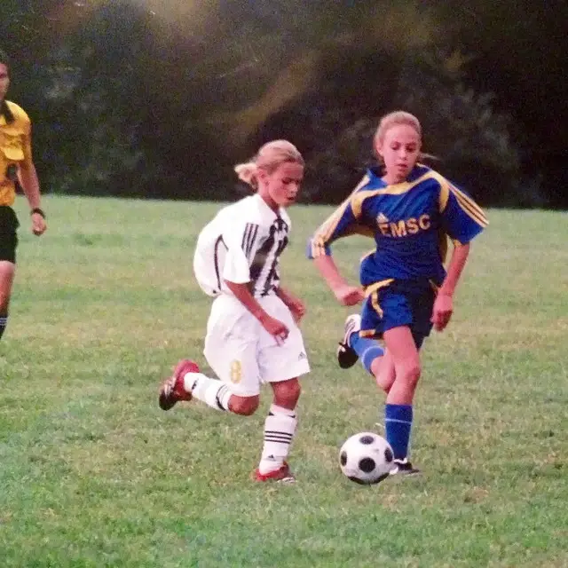 A childhood photograph shows a young Emily Fox on the left wearing a white soccer jersey and white headband, standing beside a teammate in a red and blue jersey.