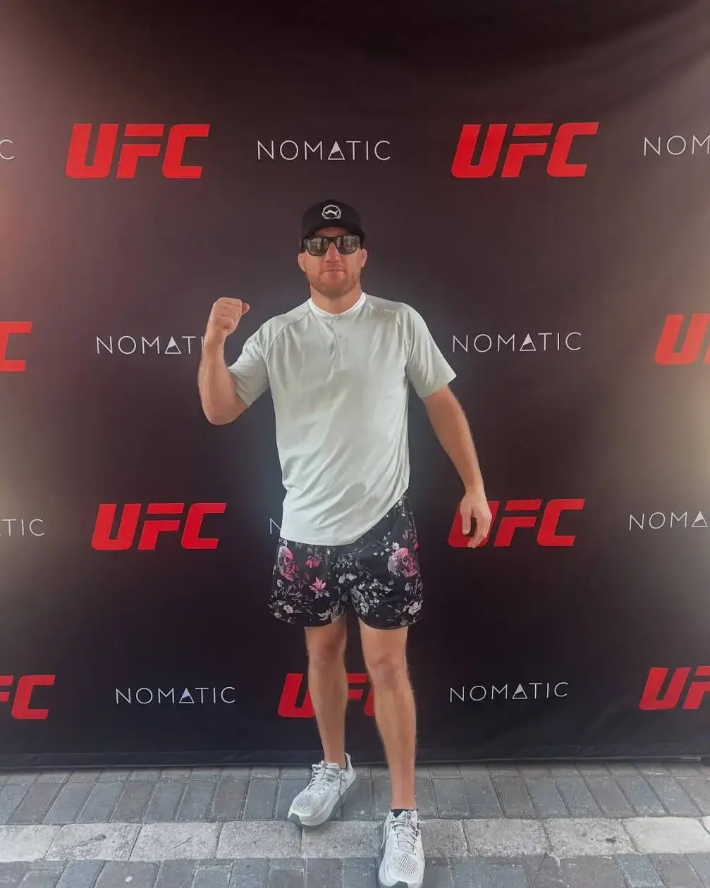 Justin Gaethje stands confidently in front of a black UFC backdrop, wearing his official fight kit and looking forward with a neutral expression.