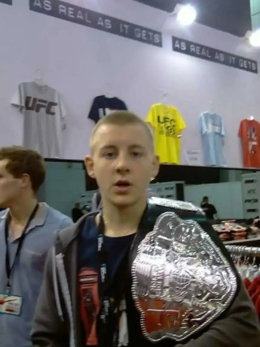 Young Pimblett stands in a merchandise area with a silver championship belt draped over his shoulder.