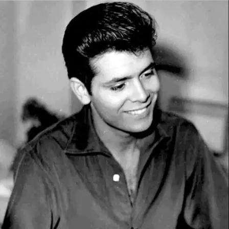 black-and-white portrait shows a young Cliff Richard smiling and looking downward with his hair styled in a classic pompadour.