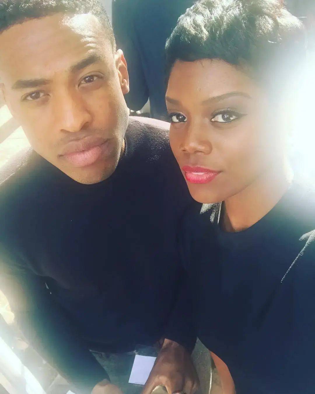 Actors Titus Makin Jr. and Afton Williamson pose closely together for a bright, sun-drenched selfie while wearing matching black tops.