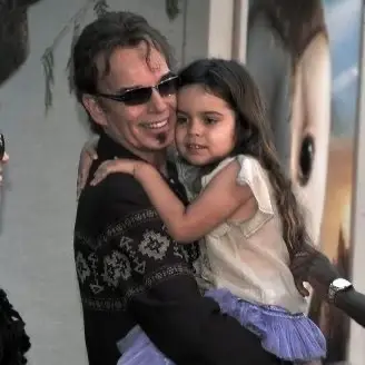 Actor Billy Bob Thornton smiles warmly while holding his young daughter, Bella Thornton, who is wearing a purple tutu, at a public event.