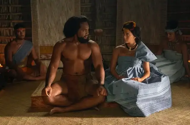 Actors Luciane Buchanan and Kaina Makua, in period costume as Queen Kaʻahumanu and King Kamehameha I, share an intense and focused conversation on the historical set of Chief of War.