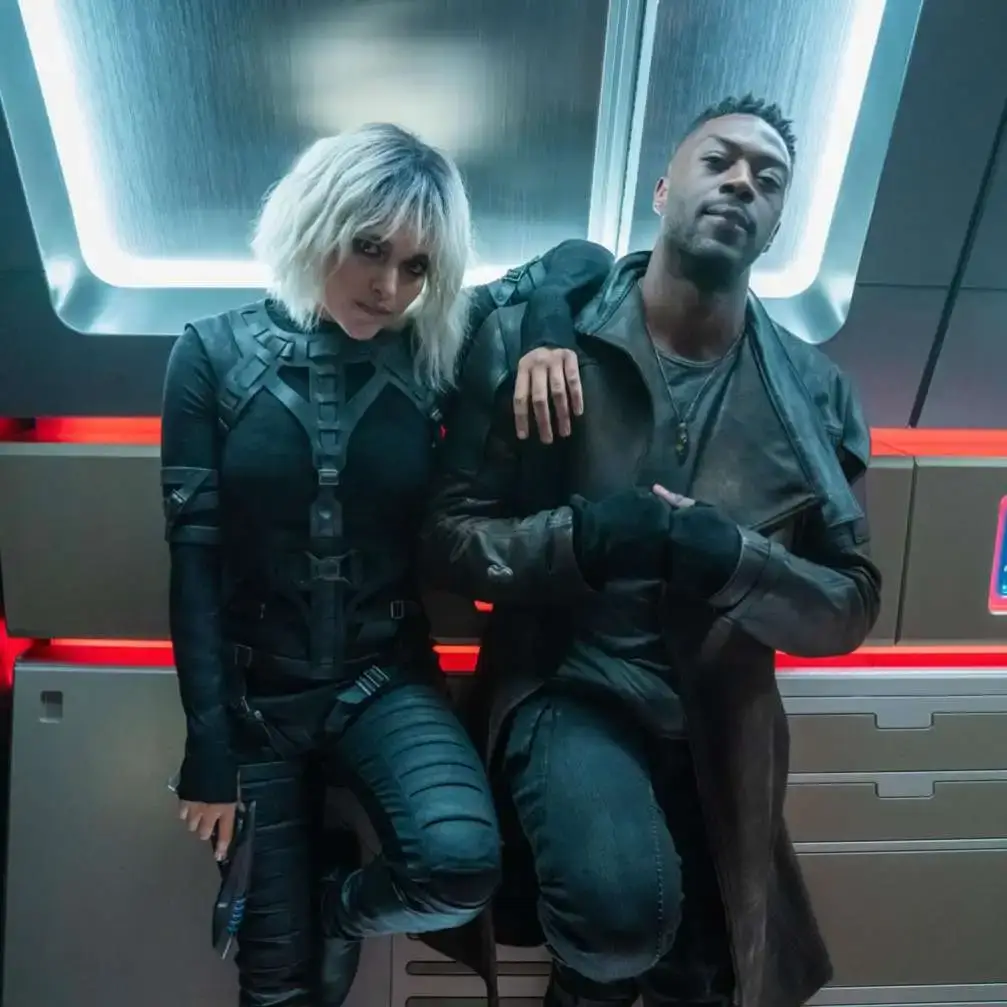 Actors Eve Harlow and David Ajala, dressed in futuristic sci-fi costumes as Moll and Cleveland Booker, stand together on the set of Star Trek: Discovery.