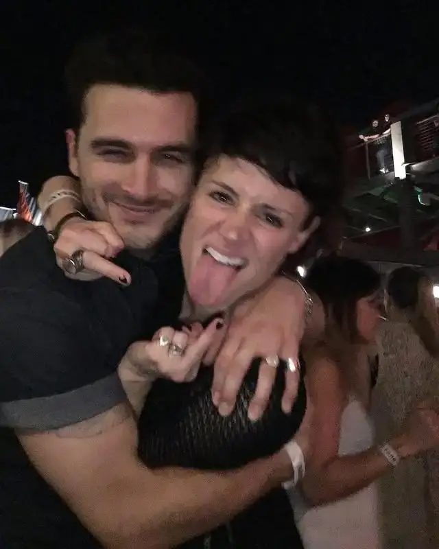 Michael Malarkey hugs his wife Nadine Lewington from behind while she playfully sticks her tongue out at the camera.
