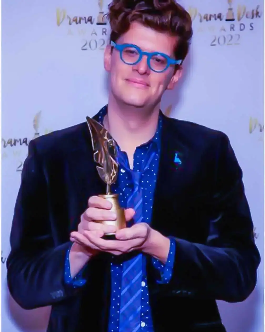 James Ortiz smiles while holding a gold trophy in front of a 2022 Drama Desk Awards backdrop.