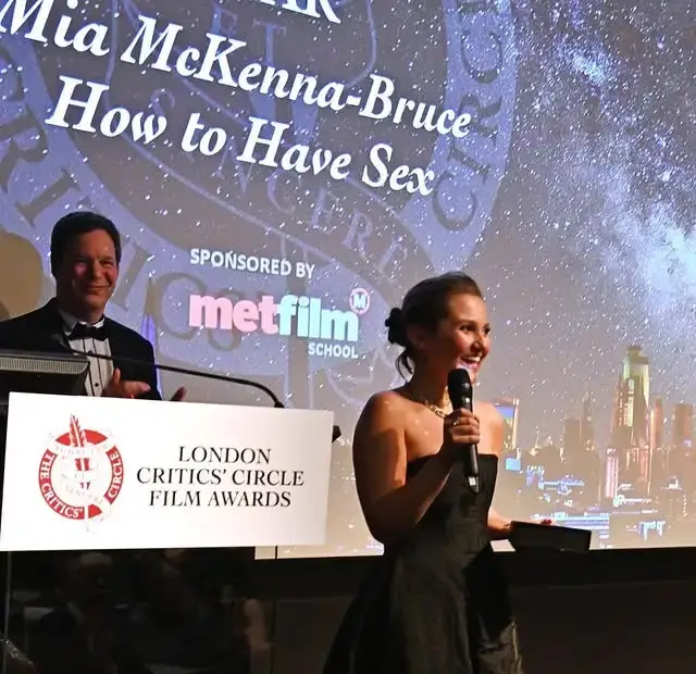 Mia McKenna-Bruce smiles brightly while holding a trophy and speaking into a microphone at the London Critics