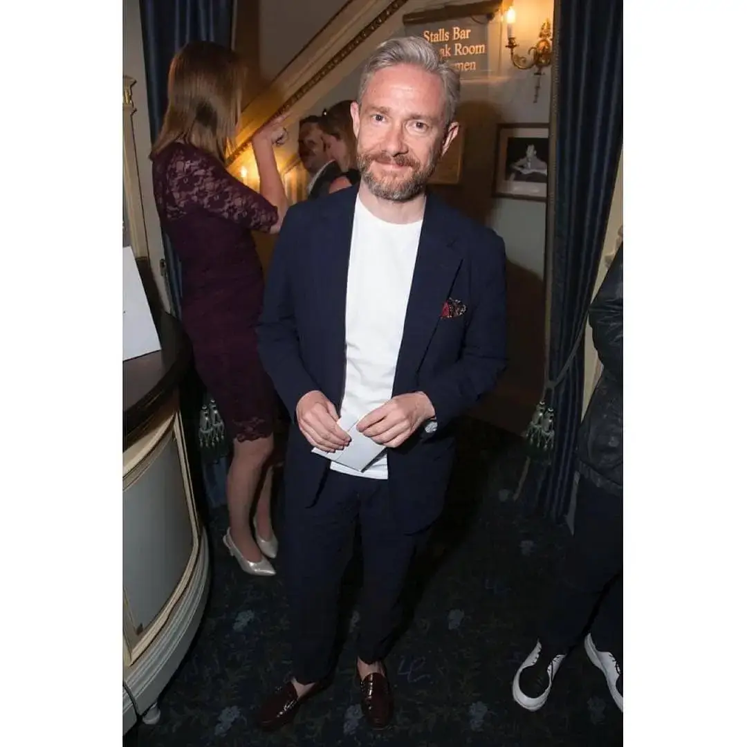 Martin Freeman smiles and wearing a dark grey suit and a light blue patterned tie.