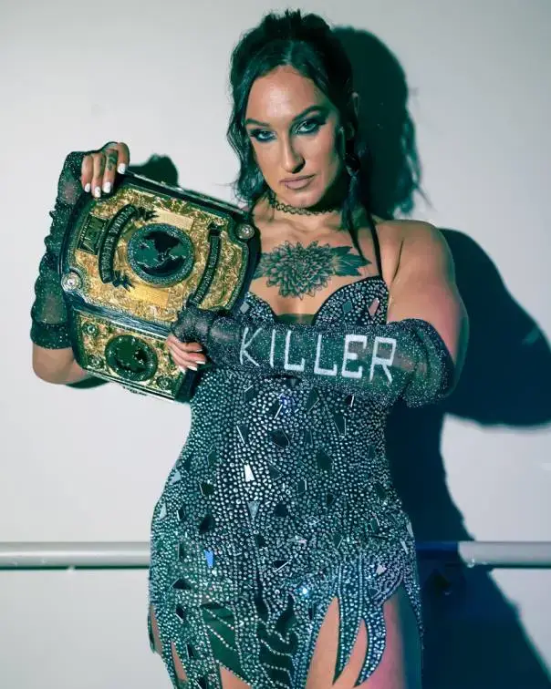 Kris Statlander stands in a wrestling ring wearing star-patterned black and silver gear while proudly holding the AEW Women