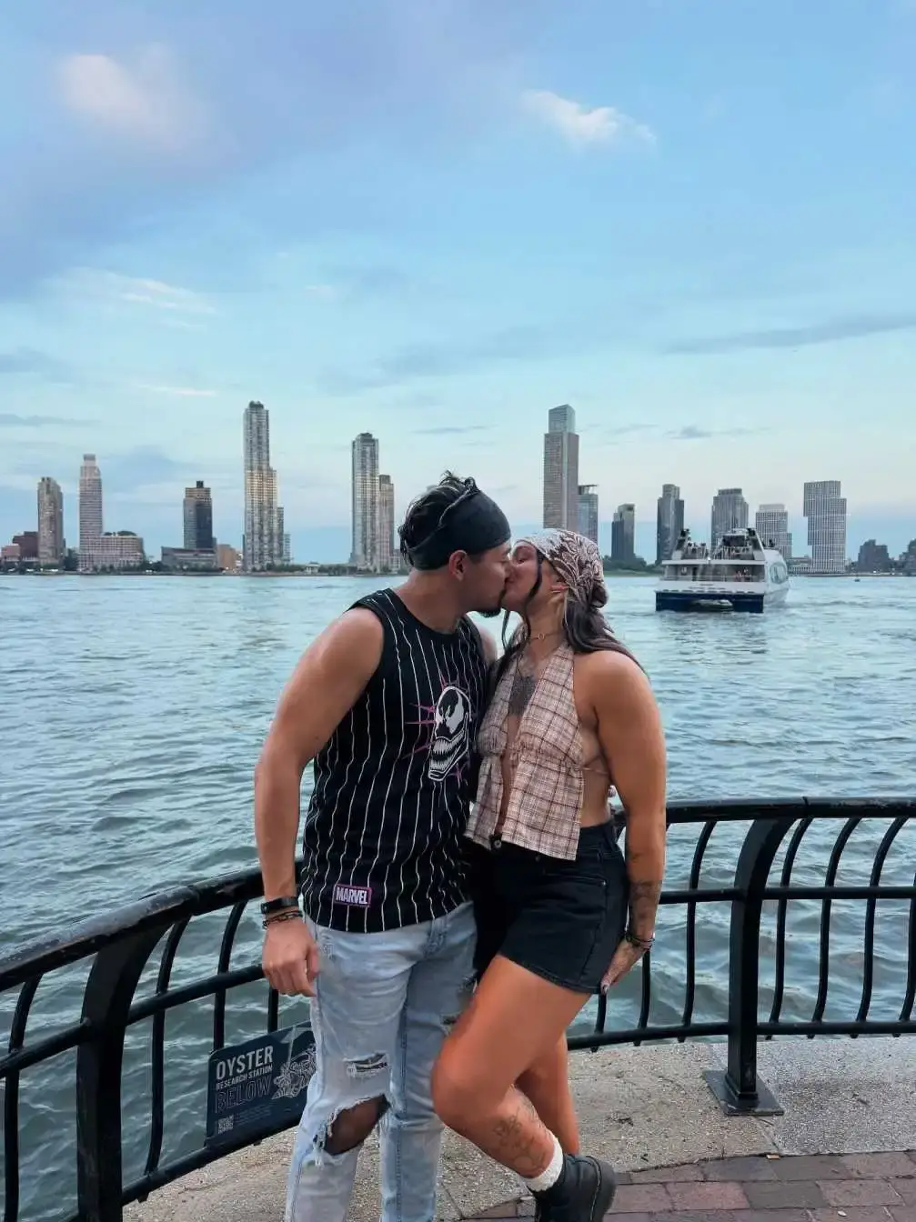 Professional wrestlers Kris Statlander and Gino Medina share a romantic kiss on a boardwalk with a city skyline and water in the background. (Image Source: callmekrisstat Instagram)