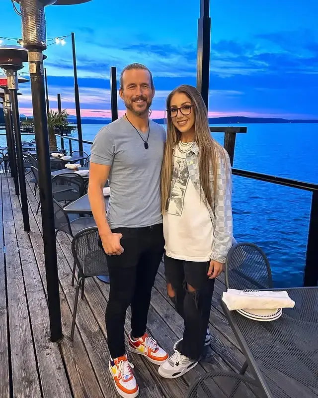 Professional wrestlers Britt Baker and Adam Cole pose together for a photo, both smiling as Cole rests his arm around Baker
