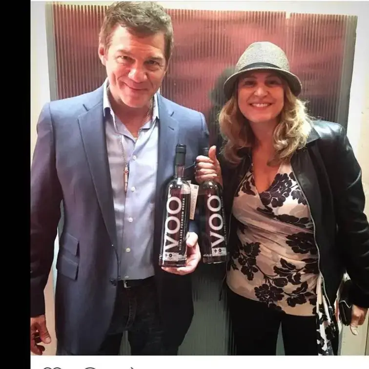 Anita Barone and Matthew Glave stand together smiling while each holding a bottle of Voo Vodka in a well-lit indoor setting.