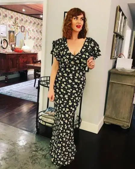 Actress Sara Rue wearing a black and white floral maxi dress in a home setting.
