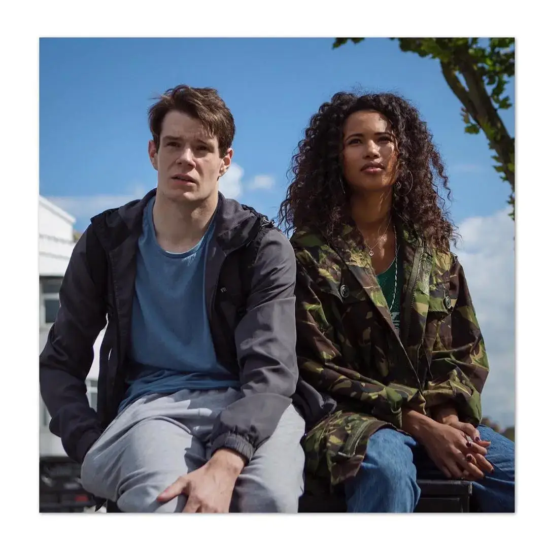 Connor Swindells and Fola Evans-Akingbola sit together on a brick wall in a casual urban setting.