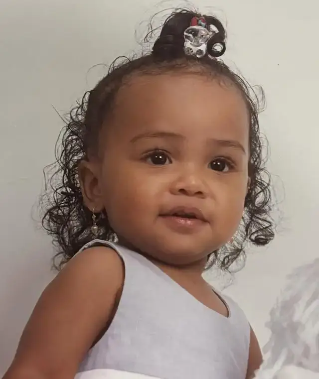 A close-up childhood portrait of Genneya Walton as a toddler with curly hair and a decorative hair clip.