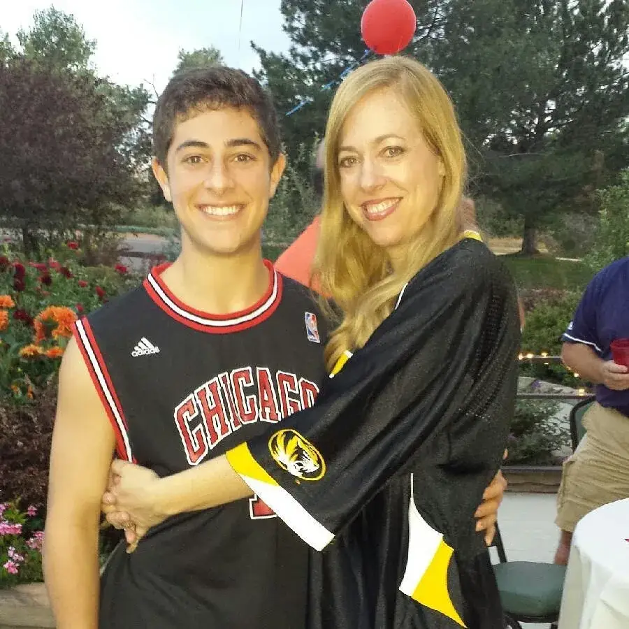 A young Jaren Lewison wears a black Chicago Bulls jersey while being hugged by his mother in an outdoor garden setting.