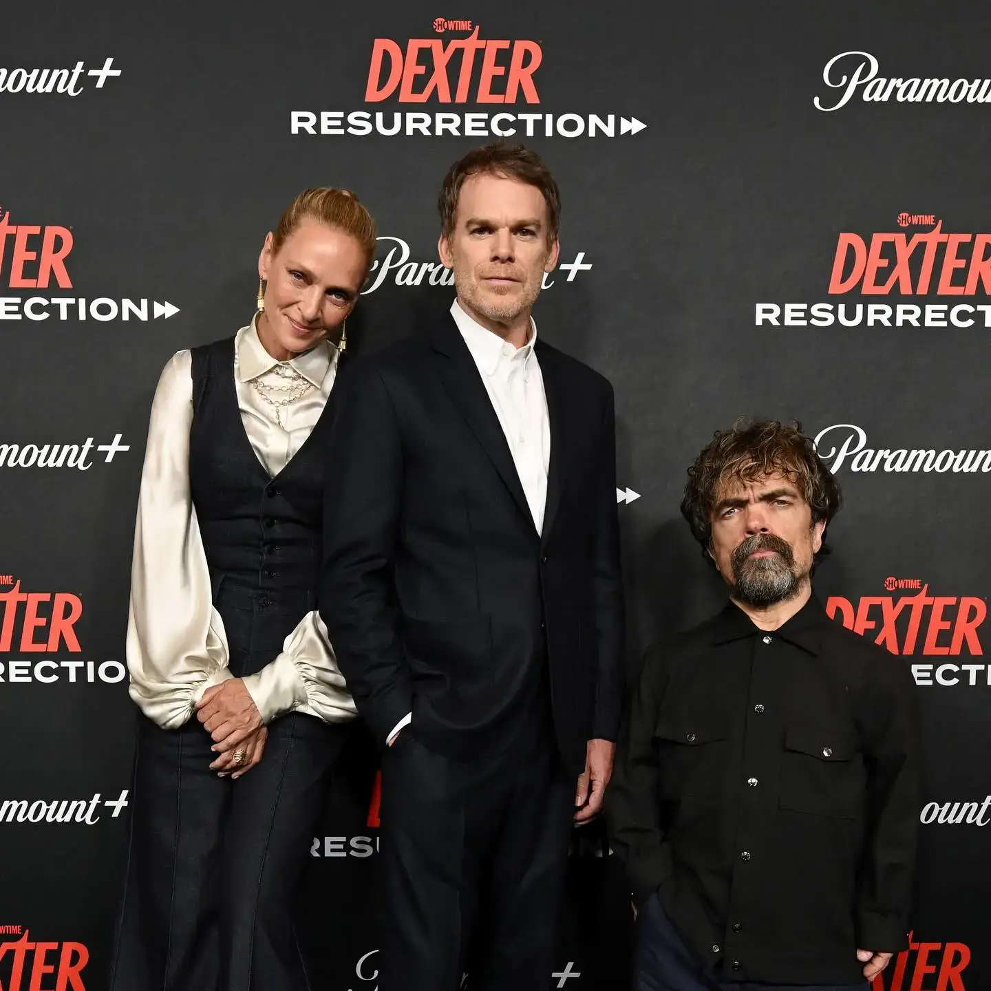 Uma Thurman stands smiling alongside co-stars Michael C. Hall and Peter Dinklage at the world premiere of Dexter: Resurrection.