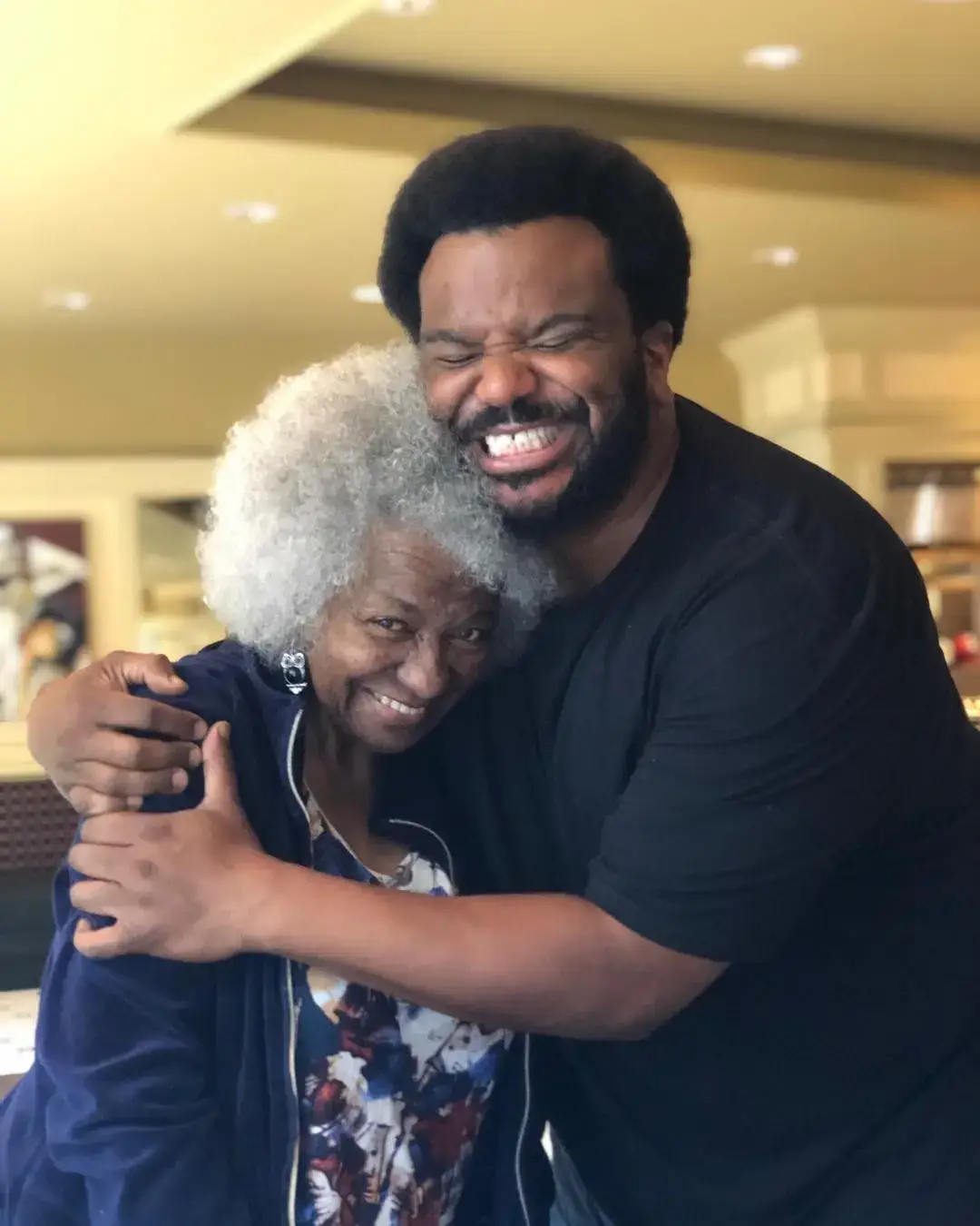 Craig Robinson shares a joyful hug with Marian Shields Robinson as they both smile warmly for a close-up photo.