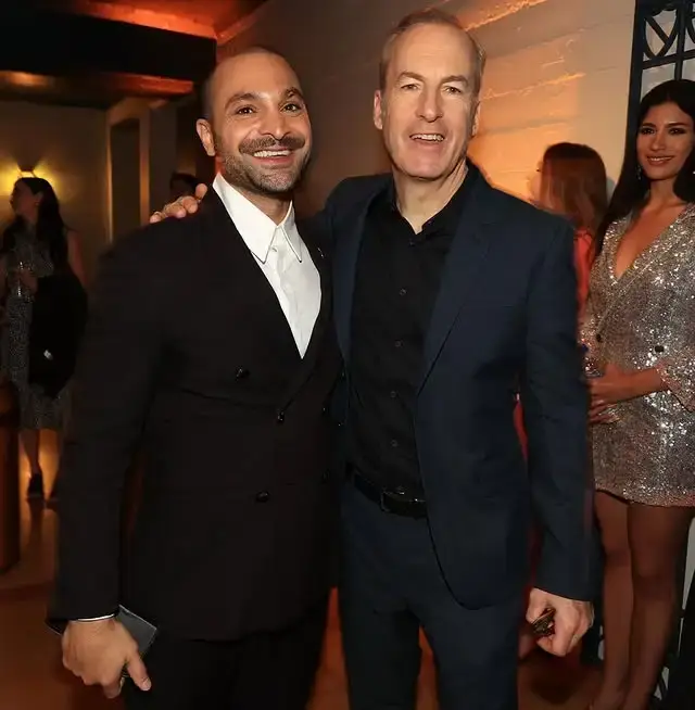 Actors Michael Mando and Bob Odenkirk smile and pose together at a formal indoor event.