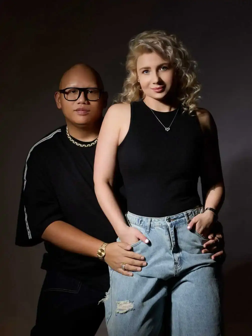 Veronica Leahov and Jacob Batalon pose for a studio portrait against a dark grey background.