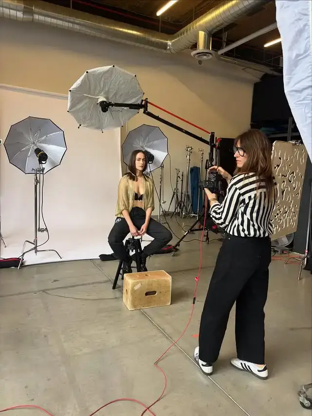 Melanie Scrofano sits for a professional photo shoot in a studio equipped with umbrellas and lighting gear.