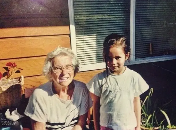 A vintage childhood photo of Frankie Adams standing next to her grandmother outdoors on a sunny day.