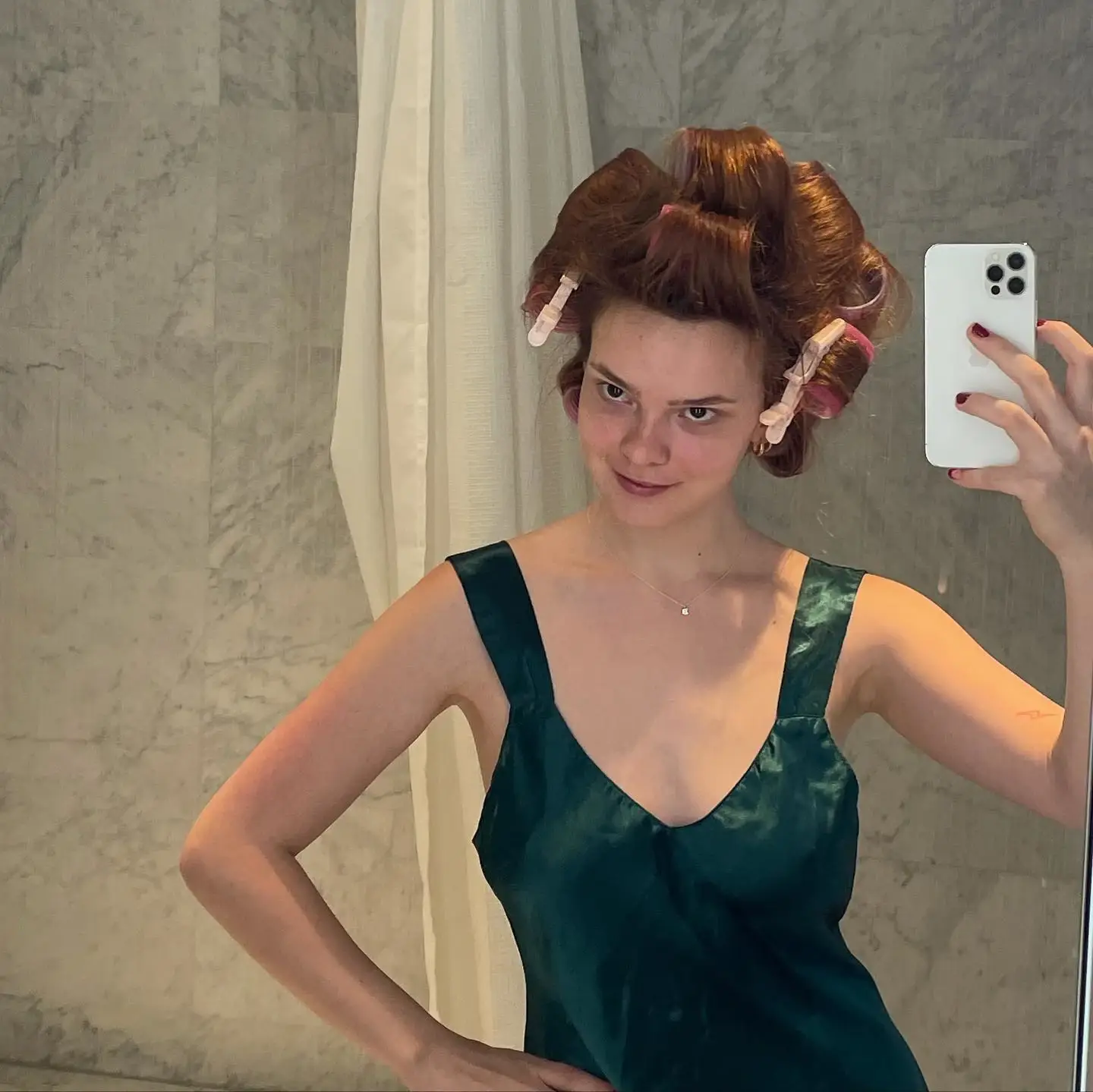 Laurel Marsden takes a mirror selfie in a green satin dress with her hair styled in large rollers.