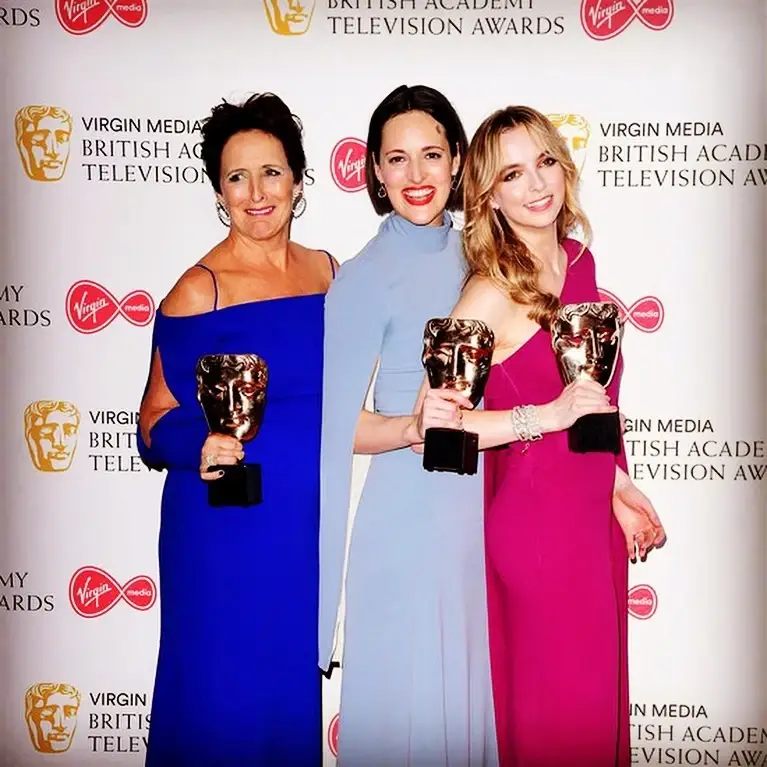 Fiona Shaw, Phoebe Waller-Bridge, and Jodie Comer pose together in vibrant gowns while holding their BAFTA awards.