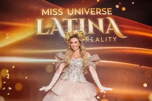 Aracely Arámbula wears a gold crown and ornate gown while standing in front of a "Miss Universe Latina Reality" backdrop.