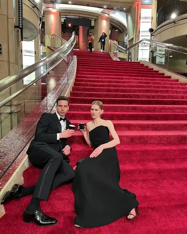 Herbert Nordrum and Iselin Steiro sit on a grand red staircase in formal black attire while holding small cups.