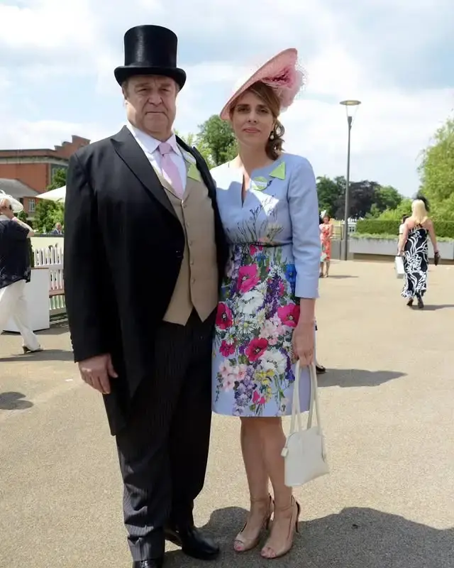 John Goodman and Anna Beth Goodman stand together outdoors in formal attire, with John wearing a top hat and tails.
