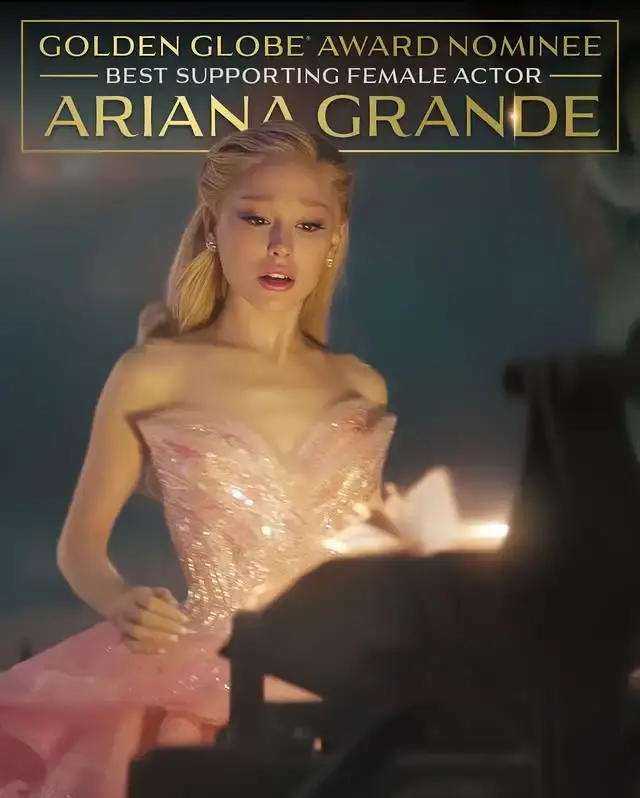 Ariana Grande stands on an awards stage in a voluminous, light pink strapless gown with large gathered sleeves.