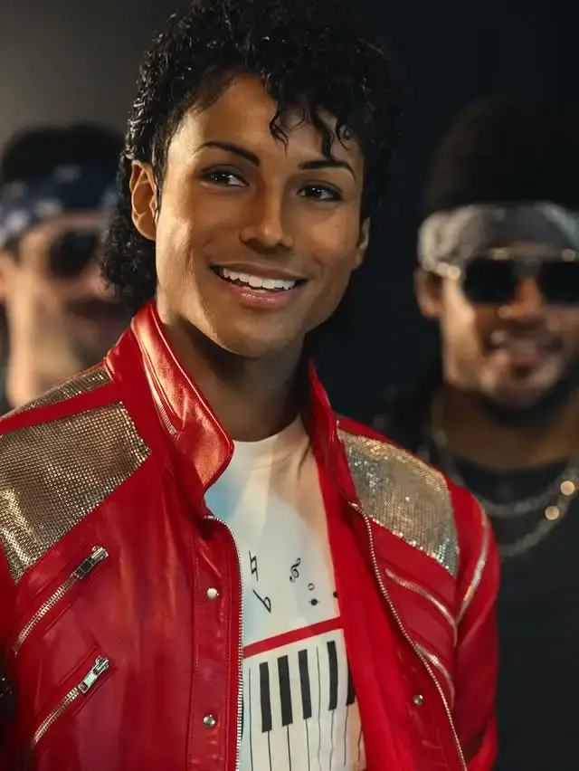 Jaafar Jackson smiles while wearing a red and gold Michael Jackson-inspired jacket with a keyboard-print t-shirt.
